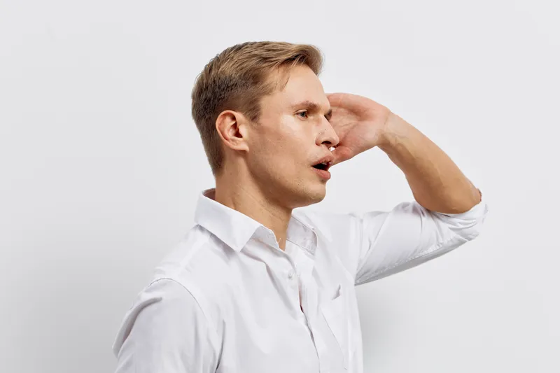 Young man in white shirt looking aside touch face isolated on light background thoughtful expression digital detox concept tech lifestyle