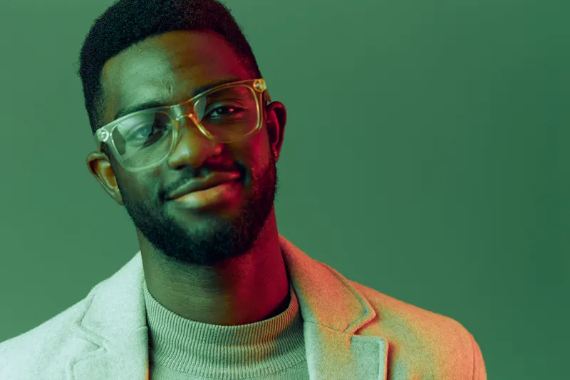 Confident Black man smiling in stylish attire, showcasing modern fashion trends in a vibrant green background with soft lighting