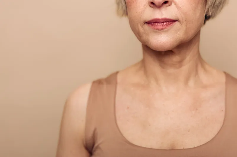 Close-up of mature woman chest and neck with natural skin texture and wrinkles visible, wearing a sleeveless top. Concept of aging, skin care, beauty, and natural appearance for health awareness.