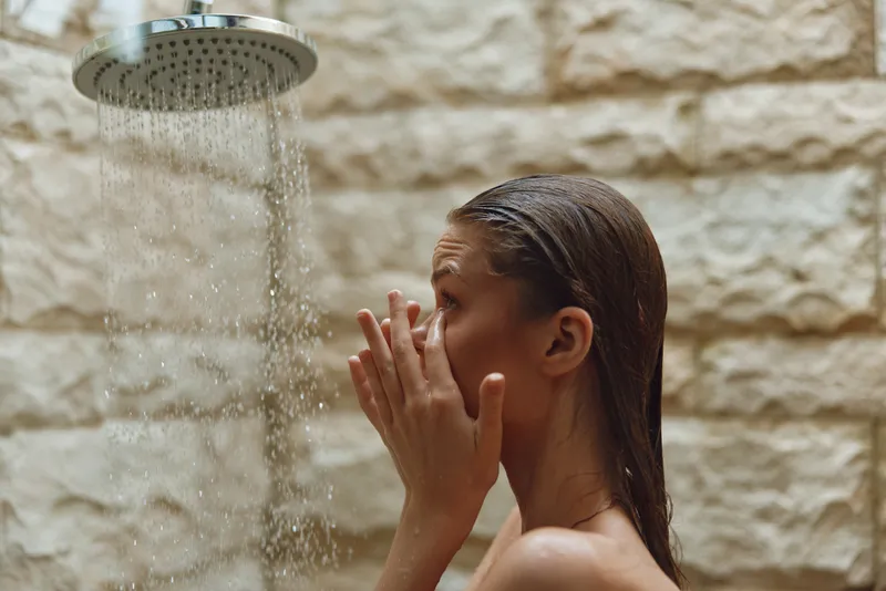 young woman washing face under shower with water drops, natural skin care, wellness routine, indoor bathroom, relaxation moment