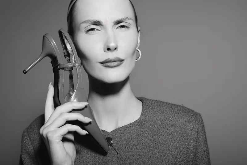 Portrait of a fair skinned Caucasian woman holding a high heel shoe to her ear as if using it like a phone. Concept for fashion, creativity, and alternative communication.