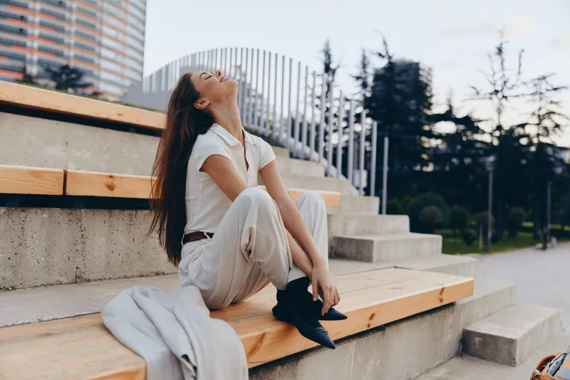 Confident businesswoman seated outdoors, showcasing modern style and serene emotions in a contemporary urban setting, emphasizing professionalism and elegance.