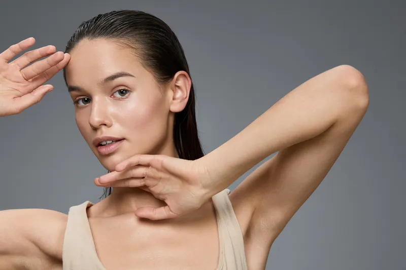 Elegant woman with wet hair showcasing natural beauty, wearing a simple beige tank top, expressing calm emotions against a neutral background