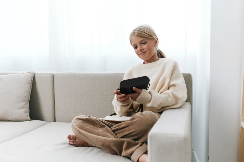 Authentic scene of a student at home, immersed in a handheld game device, blending study, focus, and play in a cozy living room atmosphere for a balanced lifestyle portrayal.