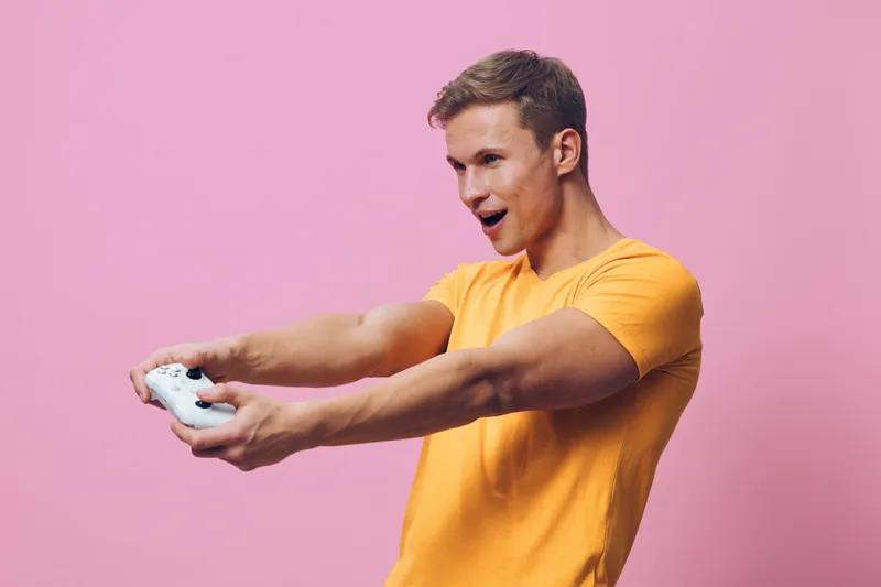 young caucasian man orange t-shirt excited play video game controller pink background digital entertainment concept