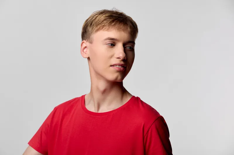 Man wearing a red t shirt looks to the side in a clean studio setting, casual style with soft lighting and neutral background, minimal styling, contemporary mood and thoughtful gaze