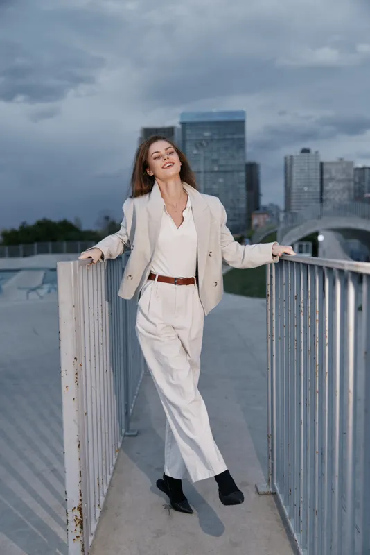 Confident businesswoman in stylish outfit poses outdoors with city skyline background, showcasing modern professional attire and a sense of empowerment.