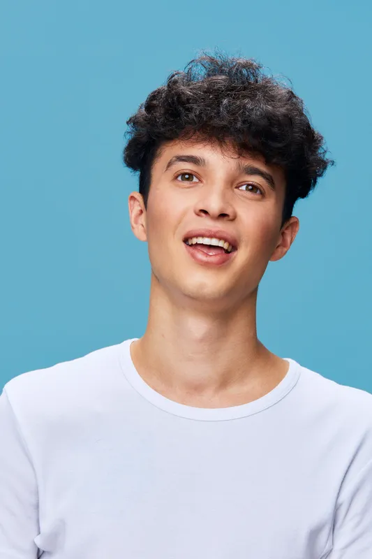smiling man with curly hair wearing white T-shirt on blue background, casual style, cheerful expression, youthful, studio portrait, modern look