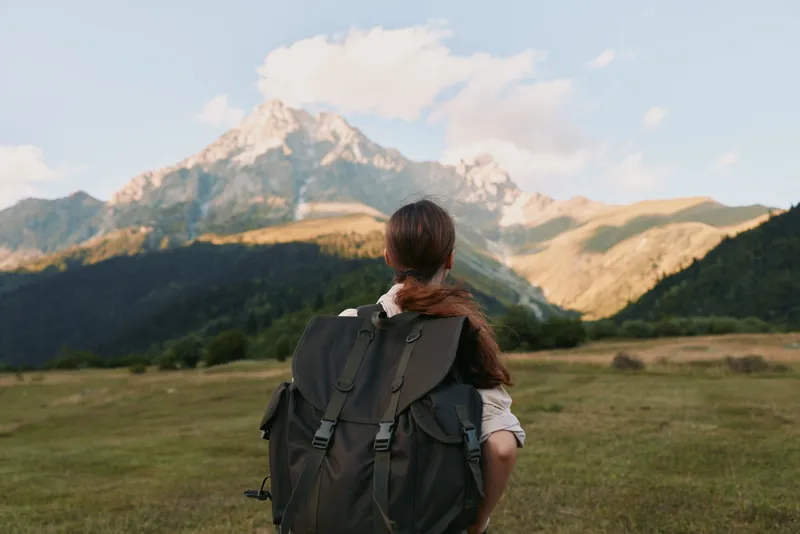 Couple hikers embrace in a wide meadow as rugged mountains rise, highlighting outdoor travel, companionship, and tranquil nature in a bright alpine landscape and weekend escape