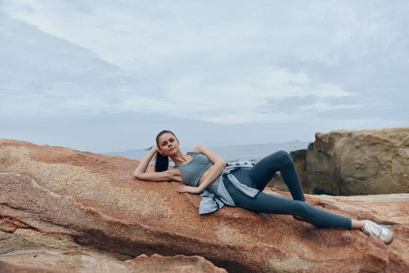 Young athletic woman in sportswear relaxing on rocky beach, showcasing healthy lifestyle and fitness, with a serene ocean background