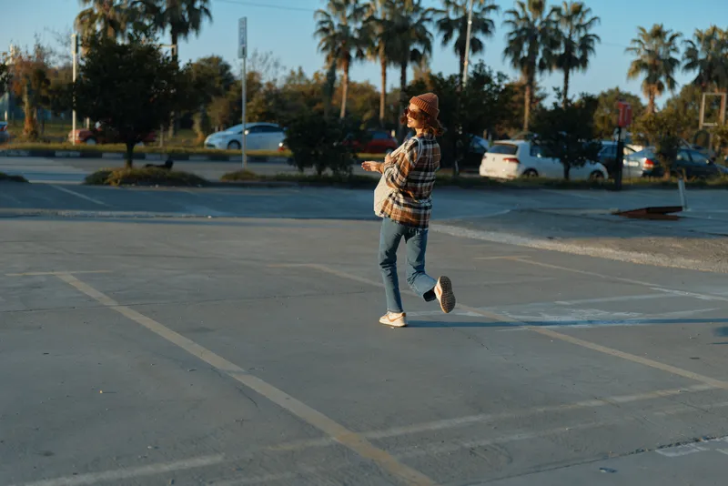 Woman walking across an empty parking lot in golden hour, candid lifestyle scene with casual urban styling, authenticity, golden hour glow, mindful living and emotional storytelling.