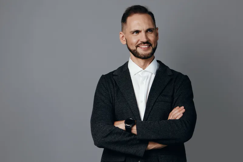 A confident business professional stands with arms crossed against a plain colored backdrop, projecting authority and approachability. The isolated background highlights leadership and expertise