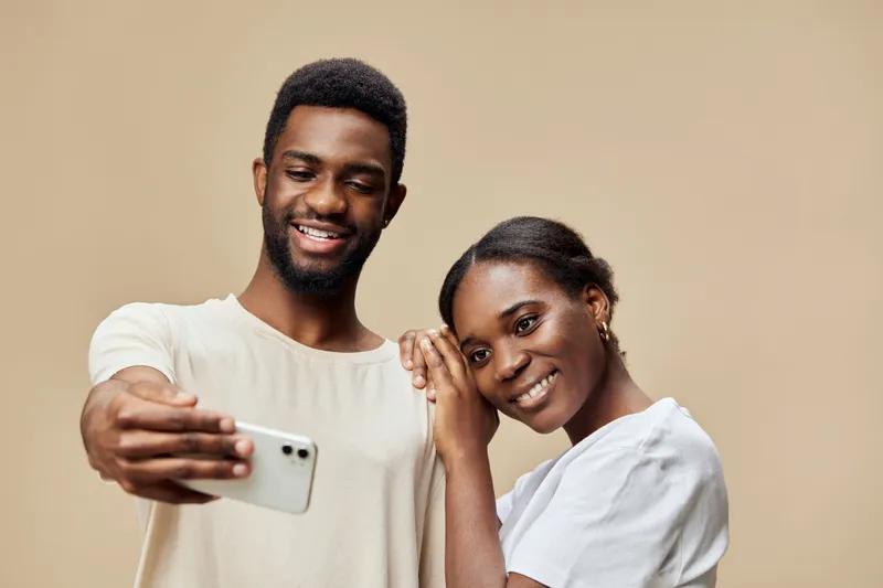 Happy couple taking selfies together, showcasing love and connection with a neutral background and warm color palette