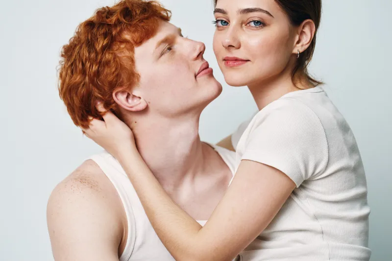 Couple, young man and woman embracing with affection in studio. Intimate, loving pair with casual white clothing and close connection, friendship and romance.