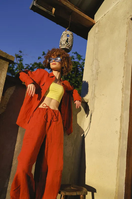 Vibrant woman lifestyle outdoors, wearing a red suit and yellow crop top, leaning against a wall, sunny moment, bold fashion pose, colorful contrast
