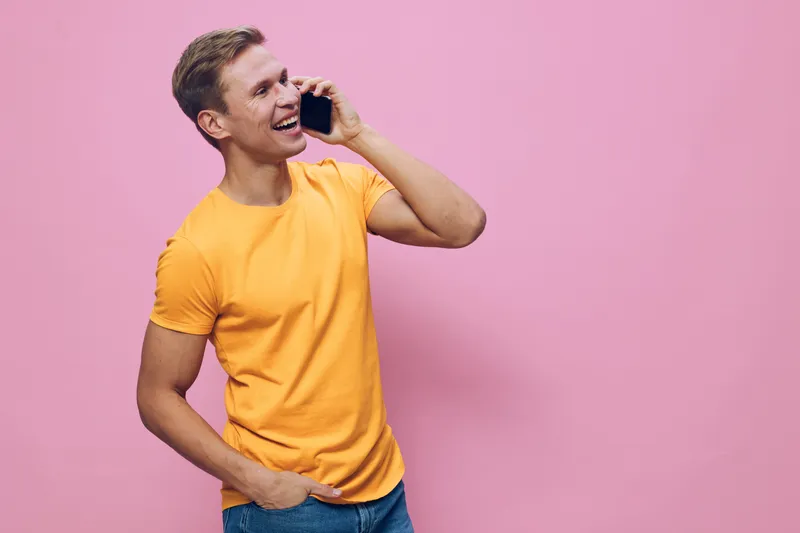 Happy smiling young man wear orange t-shirt making phone call talking with smile pink background casual style communication concept digital nomad technology