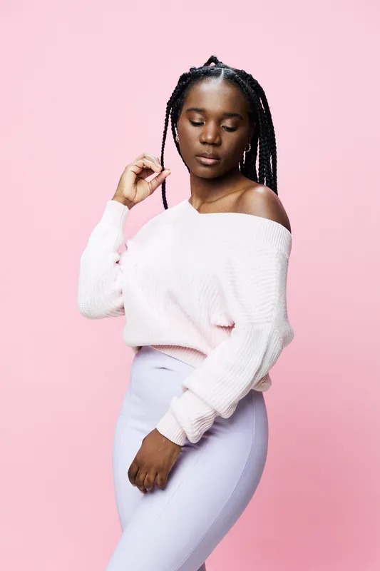 Young Black woman in pastel off shoulder sweater and leggings poses gracefully against a pink background, exuding confidence and style