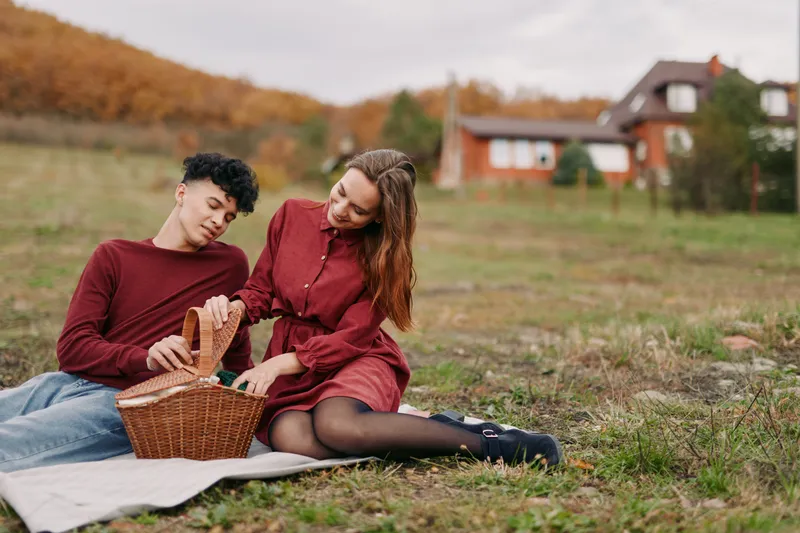 Authentic moment of a couple sharing a picnic in an autumn field, warm light, candid smiles, simple joy, natural setting, calm atmosphere, believable scene.