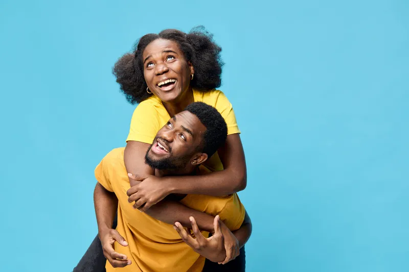 Joyful couple embracing with vibrant yellow attire against a bright blue background, symbolizing love, happiness, and playfulness in youthful relationships