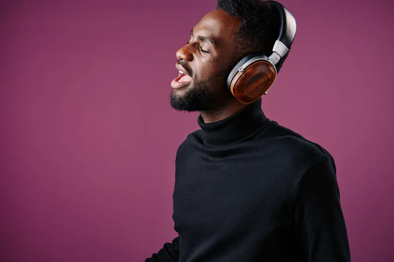 A young African American man singing joyfully while wearing stylish headphones against a vibrant purple background, showcasing happiness and passion for music