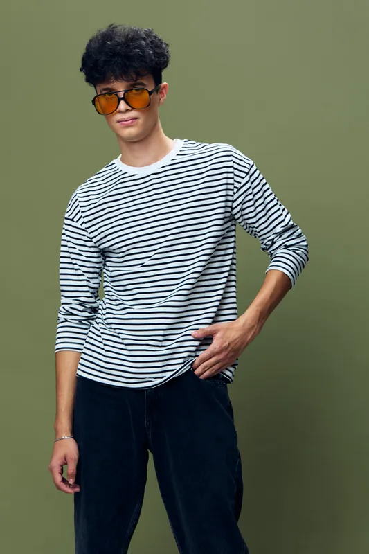 young man wearing striped shirt and tinted sunglasses posing confidently against green background in casual style with curly hair and relaxed posture
