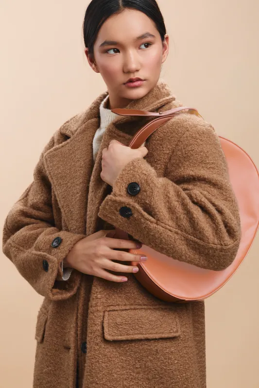 asian woman wearing a plush coat and round bag stands against a neutral backdrop, exuding style and poise with a calm, confident presence.