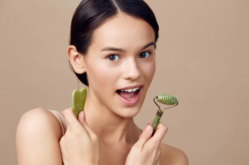 Young woman showcasing skincare tools, including jade rollers and a gua sha, promoting natural beauty and self care, suitable for health and wellness concepts