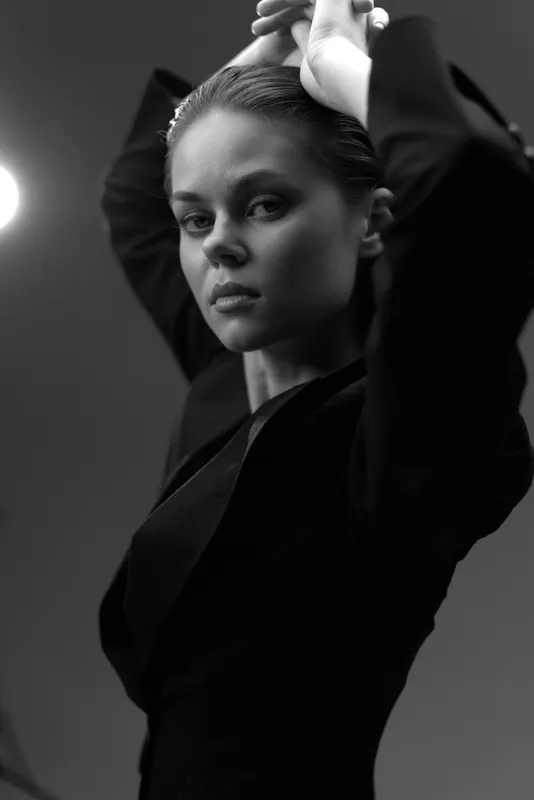 Black and white portrait of a serious woman with tied hair in elegant clothing, expressing confidence and poise in soft lighting.