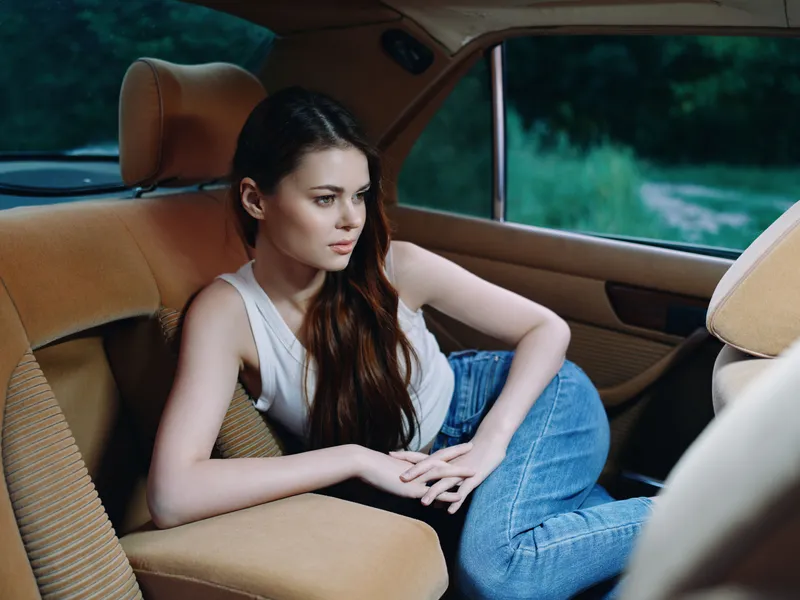 Young woman in casual outfit posing thoughtfully inside a car, showcasing emotions of contemplation and tranquility against a serene green backdrop.