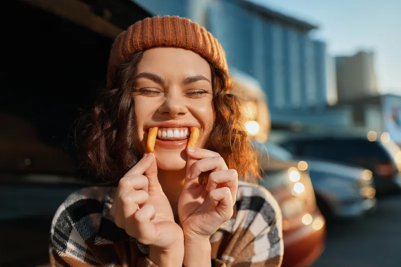 Woman smile fries candid golden beanie urban joyful lifestyle playful scene at golden hour glow, authenticity and emotional storytelling capture mindful living and spontaneous grin.