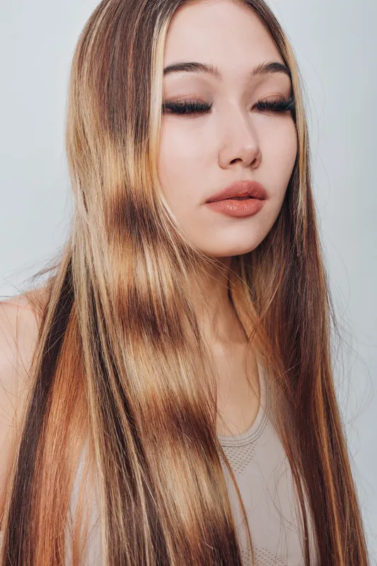 Young woman with long straight hair and closed eyes in natural look and minimal makeup on light background for beauty and fashion portrait.