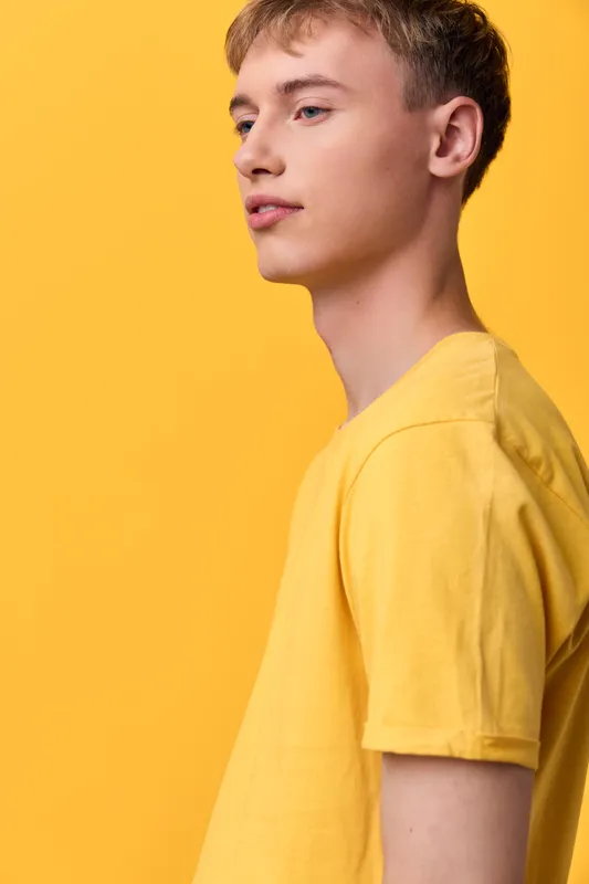 Youth in a yellow tee stands against a bright yellow backdrop, highlighting casual fashion, minimalism, and a relaxed, confident mood for modern lifestyle shoots
