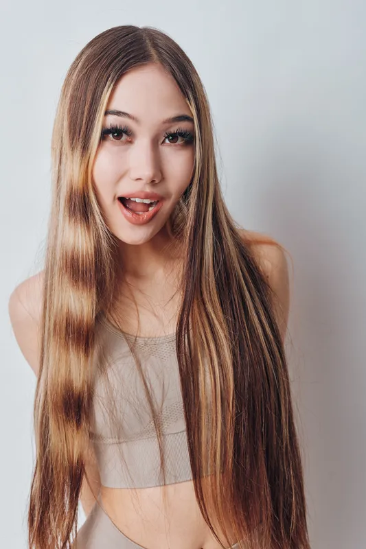 Young woman with long straight hair posing and smiling, wearing sleeveless top, portrait with natural makeup and casual style on light background.