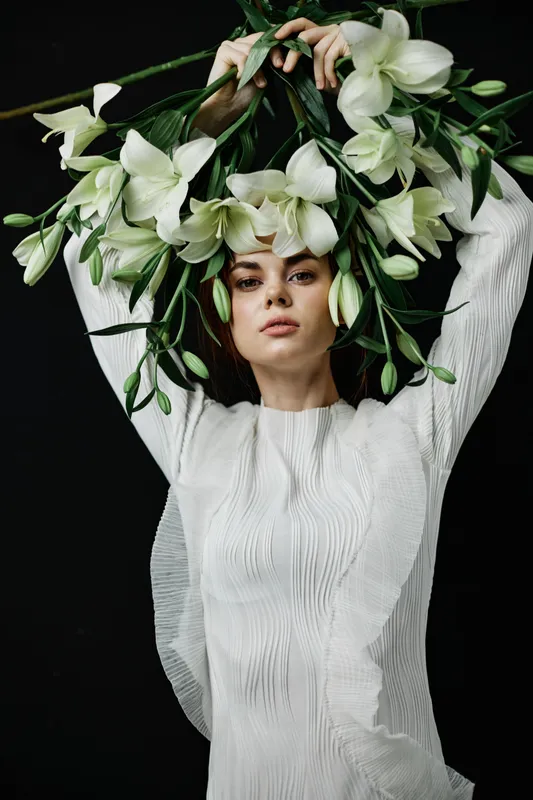 Elegant woman in a white dress holding white flowers against a dark background, expressing serenity and grace in a seasonal floral concept