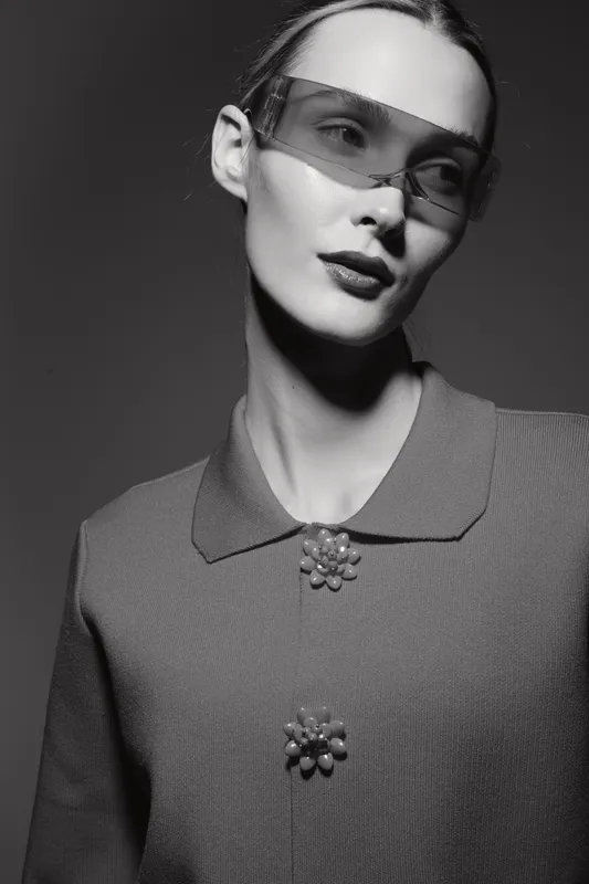 Portrait of a stylish white woman with pale skin wearing transparent glasses and a textured jacket. Studio fashion concept with soft lighting and elegant minimalism.