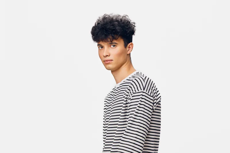 young man in striped shirt looking sideways with serious expression against plain white background, casual style, natural lighting, studio portrait