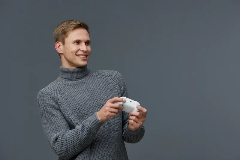 smiling man holding game controller wearing gray turtleneck sweater studio portrait casual technology concept digital entertainment joy