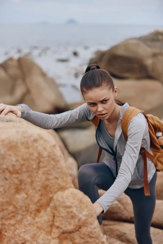 A determined woman in activewear climbs rocky terrain, showcasing resilience and strength in an outdoor adventure Ideal for fitness and motivation themes