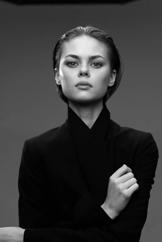 Black and white serious woman portrait in dark clothing with a minimalist background, expressing confidence and elegance.