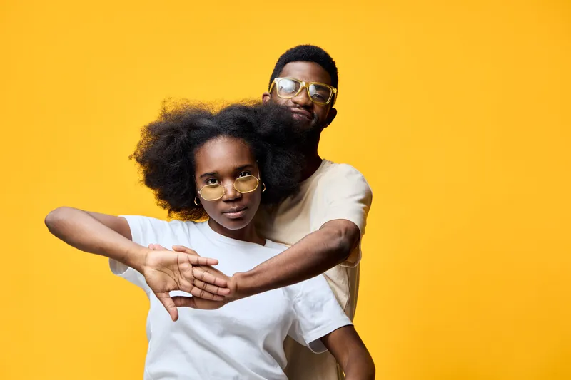 Stylish couple posing against a vibrant yellow background, exuding confidence and joy with casual outfits and trendy sunglasses, ideal for modern lifestyle concepts
