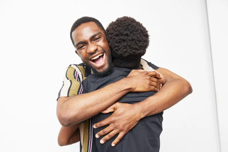 Happy African American men embracing each other, showcasing love and friendship in a joyful moment, set against a clean white background.