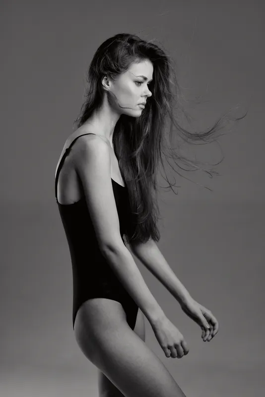 Black and white portrait of a thoughtful woman in a black bodysuit with flowing hair and neutral expression