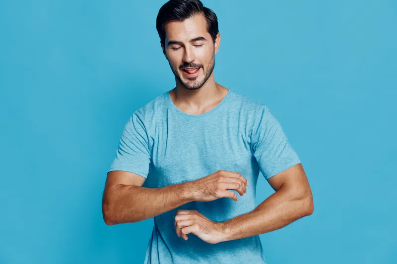Handsome young man wearing a light blue t-shirt smiling with happiness while standing against a solid aqua blue background in a cheerful studio portrait.