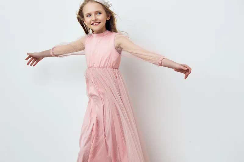 A joyful young girl in a flowing pink dress twirls gracefully with arms outstretched, capturing a sense of happiness in a minimalist setting