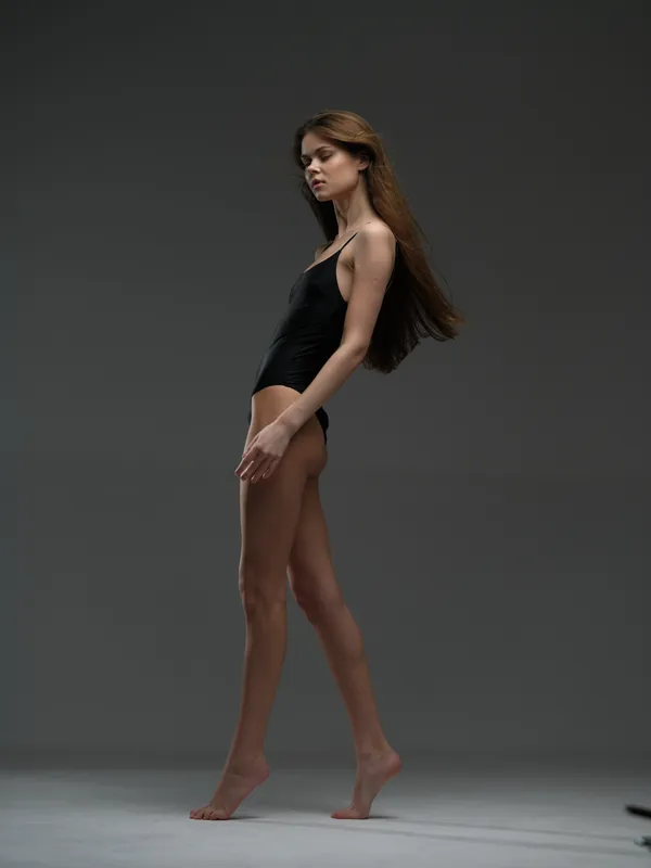slender woman in black bodysuit posing gracefully in studio with neutral background and soft lighting