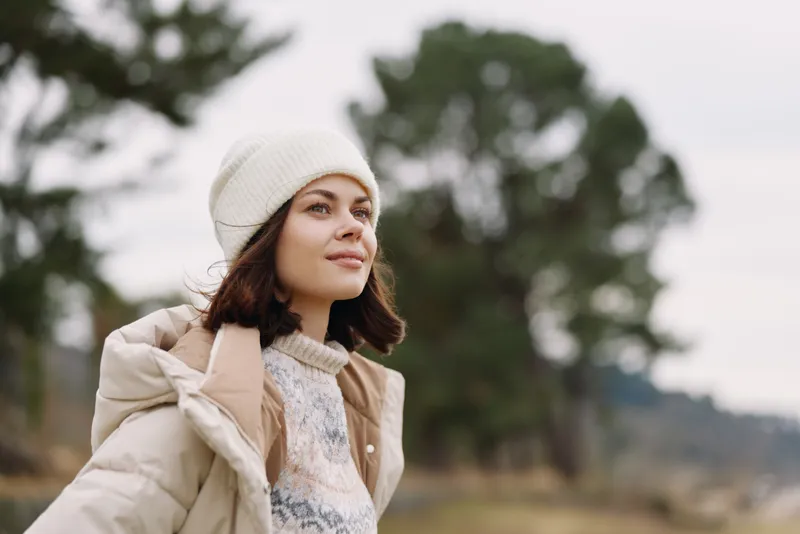 Woman in a winter coat and beanie outdoors, portrait in a natural landscape with soft light, calm mood and breeze, emphasizing outdoor style and warmth.