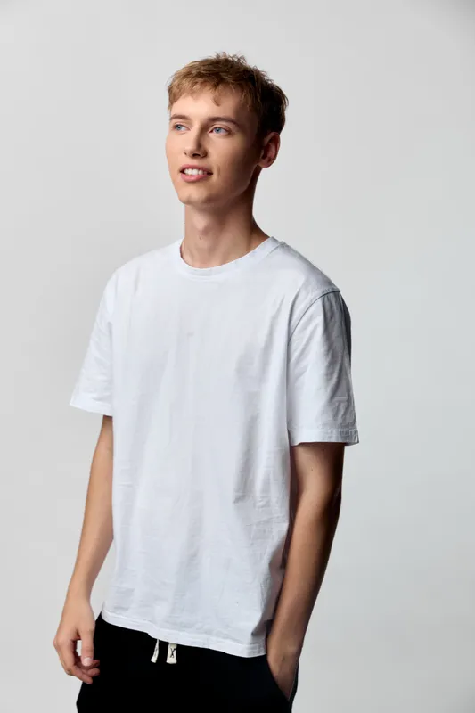 Young man in a white t-shirt stands in a studio with a clean background, showcasing casualwear and relaxed style for fashion and lifestyle shoots with a simple modern look