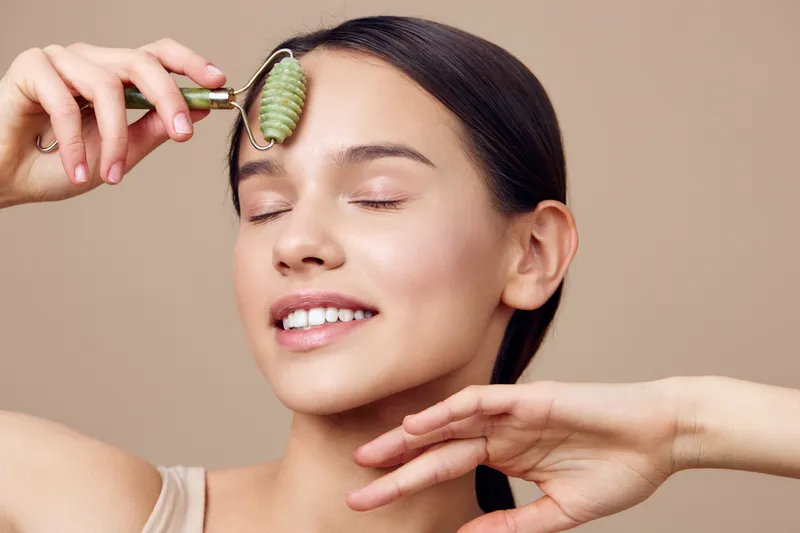 Young woman using a jade roller on her forehead, smiling softly with closed eyes, enhancing her skincare routine, natural beauty concept