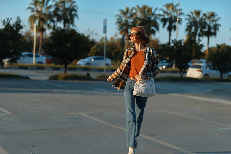 Woman walking in parking lot at sunset, casual outfit and sunlight on face, urban palms in background, authenticity and candid lifestyle, golden hour glow and emotional storytelling.