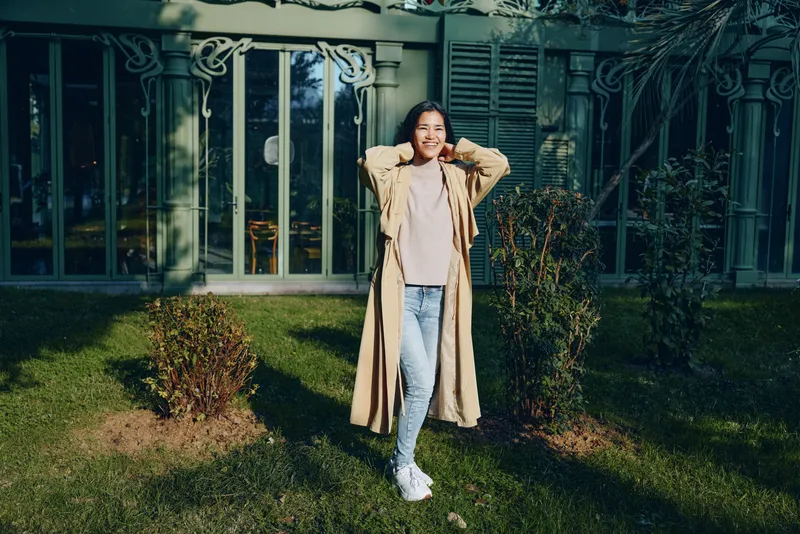 Coat, fashion, outdoor garden scene with a woman wearing a long beige coat in a sunny yard, casual street style amid greenery and a modern backdrop